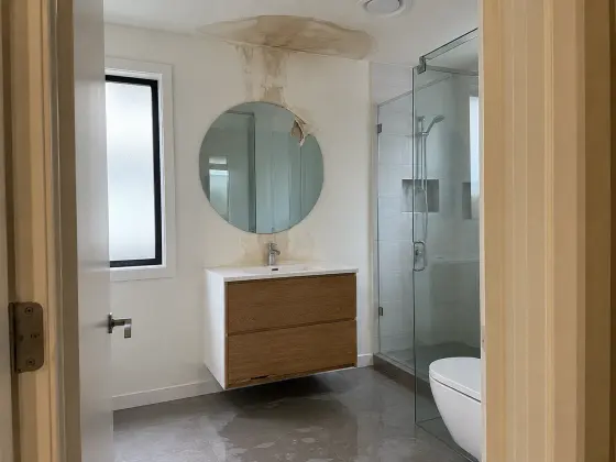 Bad mit Wasserfleck an der Decke über dem Waschtisch, Wasser auf den Bodenfliesen (KI-generiertes Beispielbild)